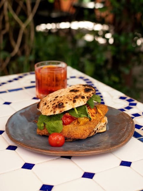 Sándwich de milanesa de hongo shiitake en pan a la leña, con rúcula y tomates confitados, sobre la mesa de la terraza